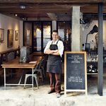Cafe owner standing outside next to a chalboard sidewalk sign